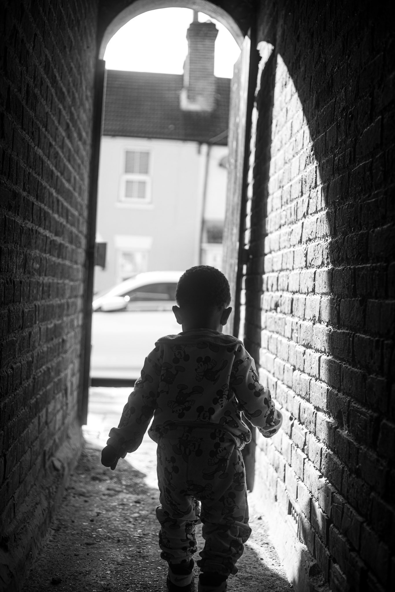 Child walking through a shadowed brick passage