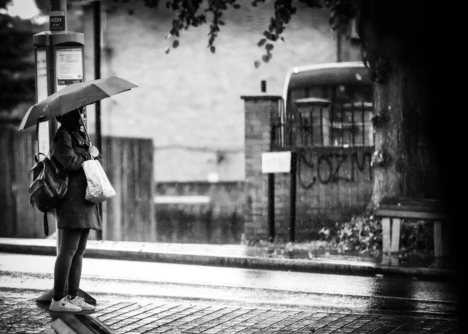 Person walking under an umbrella beside a bus stop